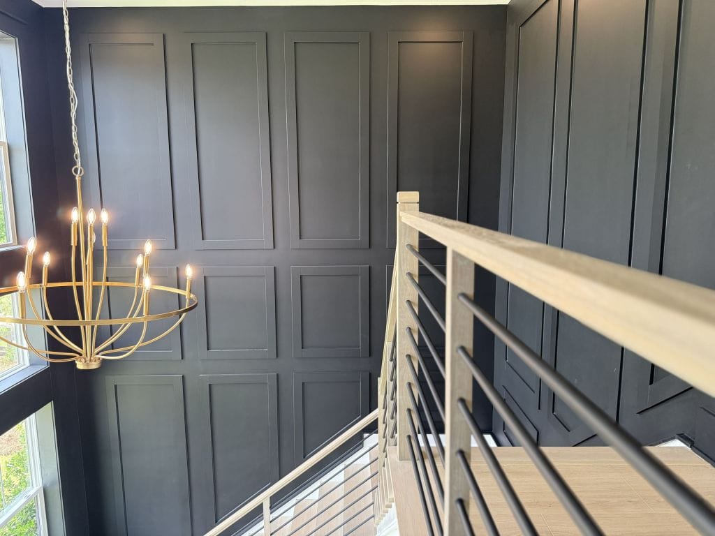 Dark two-story wall with picture-frame panel moulding above a light oak stair railing